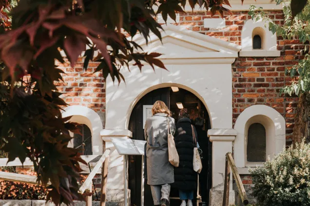 En person går in i en byggnad. Löv hänger framför kamera.