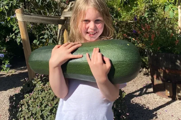 flicka i vit klänning håller en stor zuccini i händerna