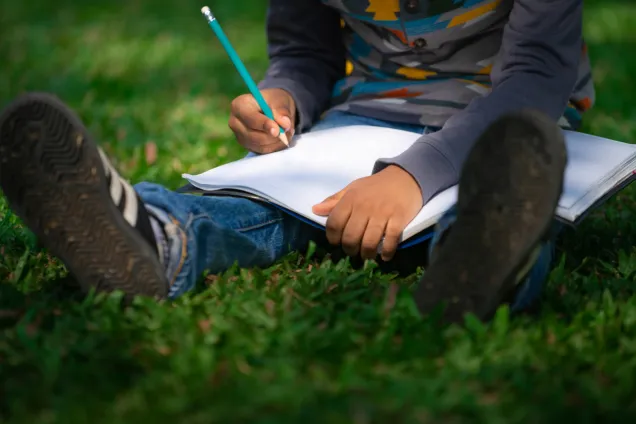 Barn som sitter i gräset och skriver