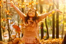 Flicka som sträcker ut händerna i höstväder med orangea löv